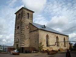 Dun-colored small squat stone church against a blue sky with clouds