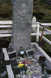  A tall stone column stands over a grave on which rest various memorabilia including a bunch of flowers. The stone is inscribed: "Ernest Henry Shackleton, Explorer, Born 15th February 1874. Died 5th January 1922".