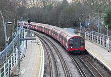 A railway platform with a railway track running through it being used by a red-and-white train with its two headlights illuminated