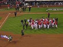 A group of men in red and white baseball uniforms gather on a baseball field.