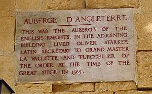 A plaque with the inscription AUBERGE D'ANGLETERRE: THIS WAS THE AUBERGE OF THE ENGLISH KNIGHTS. IN THE ADJOINING BUILDING LIVED OLIVER STARKEY LATIN SECRETARY TO GRAND MASTER VILETTE AND TURCOPILIER OF THE ORDER AT THE TIME OF THE GREAT SIEGE IN 1565