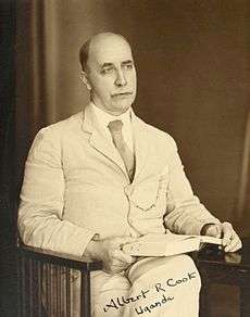 Cook seated in a wooden armchair holding a book