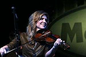 A woman wearing a brown jacket and playing a fiddle