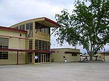 On the left, a beige two-story building with large windows. The front of the building says "Library Media Center." On the right, a smaller beige building and a large tree