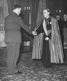 a male in archbishop's garb greeting a male in military uniform