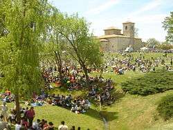 Large group of people picnicking in a parklike setting, with a church in the background