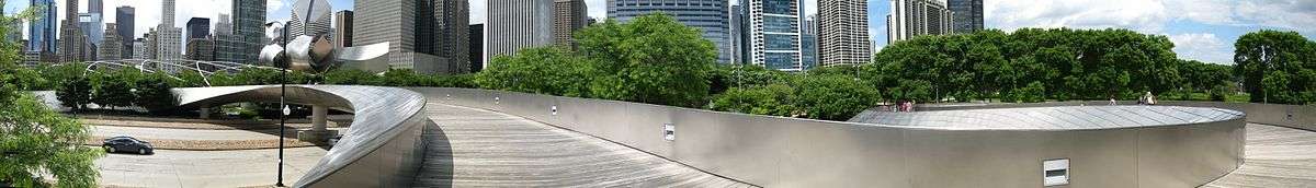 Panoramic view of a shiny metal bridge crossing a multilane road, with skyscrapers in the background.