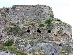 A ruined building made of stone with bushes growing from the ruins on a cliff