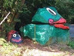 A pair of stacked rocks, painted green, with lips and eyes drawn on on the top rock.