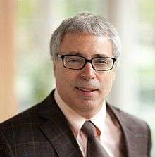 Photo of smiling, clean shaven man with glasses and grey hair