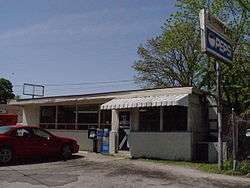 White single story building with a red car parked in front, also the restaurant's sign at photo right