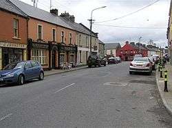 Small village street lined with houses, pubs and parked cars.