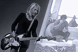 A woman plays a guitar in front of a projection screen.