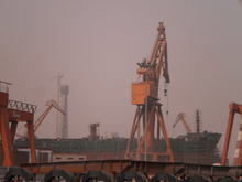 An unfinished ship and an orange crane at the center of an industrial setting