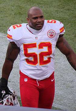 Brandon Siler, in white jersey and red pants of Kansas City Chiefs, walks to sideline carrying his helmet.