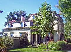 A house with curving roof and a small tree in front, seen from the side