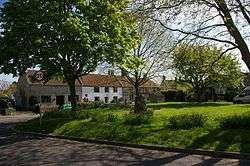 Grassy area with trees in the foregound and a terrace of stone houses, one white fronted, in the background