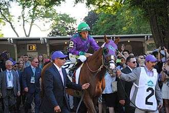 A racehorse being led by two people, one on each side, and other people nearby