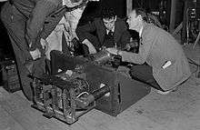 Four men in suits bend over a piece of machinery.