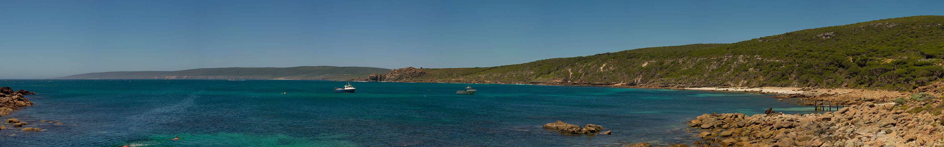 bay of water, with fishing boats at anchor, and the small town of Yallingup near the centre across the bay with hill ridge across the horizon