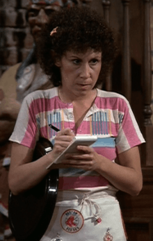 An angry-looking woman has the permanent hair with a hair ornament and the apron with the "Boston Red Sox" banner. She also holds a large drink tray under her right shoulder and a book of blank guest checks.