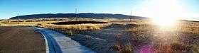 A panoramic picture of a loaf shaped mountain with the sun shining low and to the right.