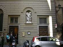 A grey-white building with a white marble statue in a niche at first floor level