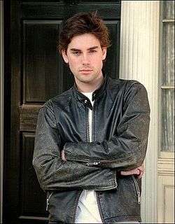 Upper body shot of handsome young man wearing a white t-shirt and black leather coat, arms are crossed