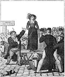 Woman standing on a raised platform surrounded by men.