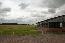 View of green, very flat field with a single story building to the right