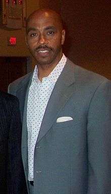 A man, wearing a gray suit and white shirt, is standing and posing for a photo.