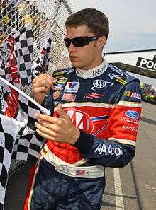 Picture of man signing his autograph on a chequered flag.