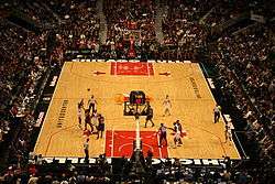 An indoor arena half-filled with people watching a basketball game.