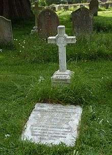 A marble horizontal gravestone at the foot of a marble cross in grassy churchyard