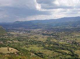 a panoramic photograph of a wide green valley with a small town in the middle distance