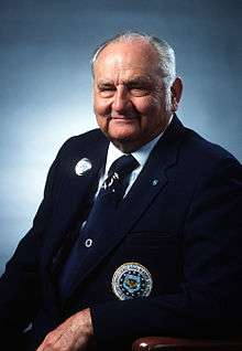 Portrait of a gray-haired white man wearing a dark blue suit and tie