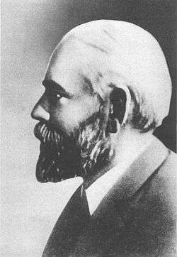 A black-and-white profile photograph of the head and shoulders of a middle-aged bearded man, facing left