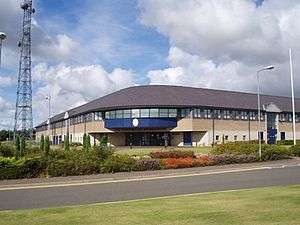 Two-storey office building made with facing brick, glass and dark blue cladding set in mature landscape