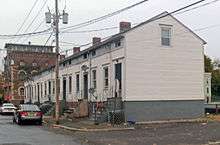 An attached row of small wooden white houses, seen from down the street