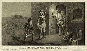 A black and white engraving, captioned "Capture of Fort Ticonderoga". Two men, one holding a lit lantern and the other with his left hand raised and a sword in his right hand, stand in the center, facing the doorway of a stone building to the right. A man stands in the doorway, wearing a nightgown and nightcap, and holding a lit candle on a candlestick. Behind him a woman is visible. To the right of the doorway is a small cannon or mortar. In the background on the left men in uniform are visible, as are stacked cannonballs, cannons, and a ladder leaning against a wall.