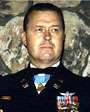 Head of a man with short, dark hair wearing a formal military uniform. Rows of ribbon bars and a winged pin are on his left breast, and a medal hangs from a light blue ribbon around his neck.