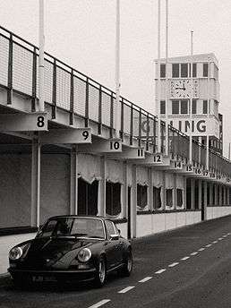 Black and white picture showing dark colours car in a pits area.