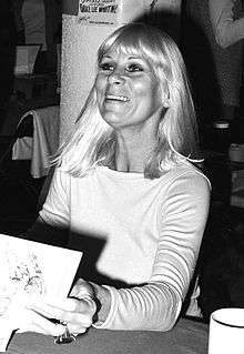 A black and white photo of a Caucasian woman sitting at a table.