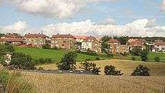 A row of red houses behind a large grassy area.