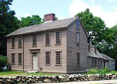 A brown two story colonial wood frame house, with an addition added on the back.