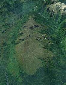 A large lightly glaciated mountain mass surrounded by vegetation and two rivers.