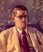 Half-length portrait of a fortyish man wearing distinctive Windsor (circular-lens) glasses with black Zylo-covered frames, short and slicked-down brown hair, a small mustache, light tan jacket and brown tie. His mouth is turned down in a slightly truculent expression