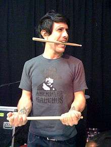 Javier Weyler biting a drum stick and holding the other in his hands