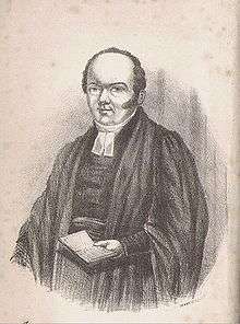 A balding clergyman in gown and clerical garb, holding an open book in his left hand