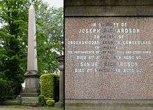 A tall obelisk made of reddish polished granite, surrounded by trees in a cemetery